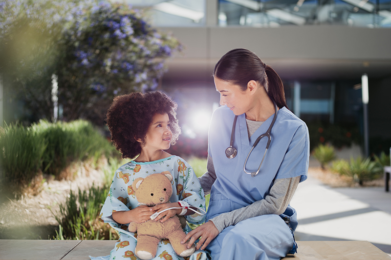 Healthcare professional with child patient holding teddy bear.