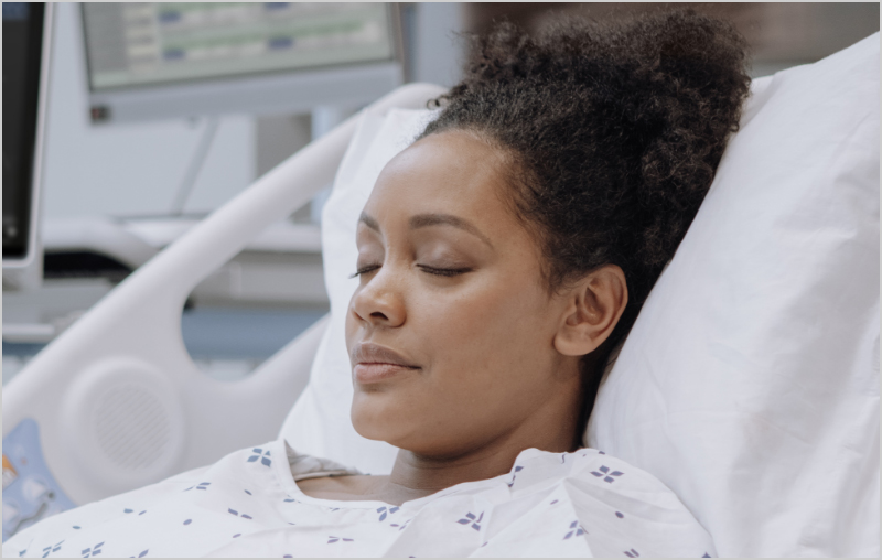 Dark-skinned patient in hospital bed monitored by Masimo Root device.